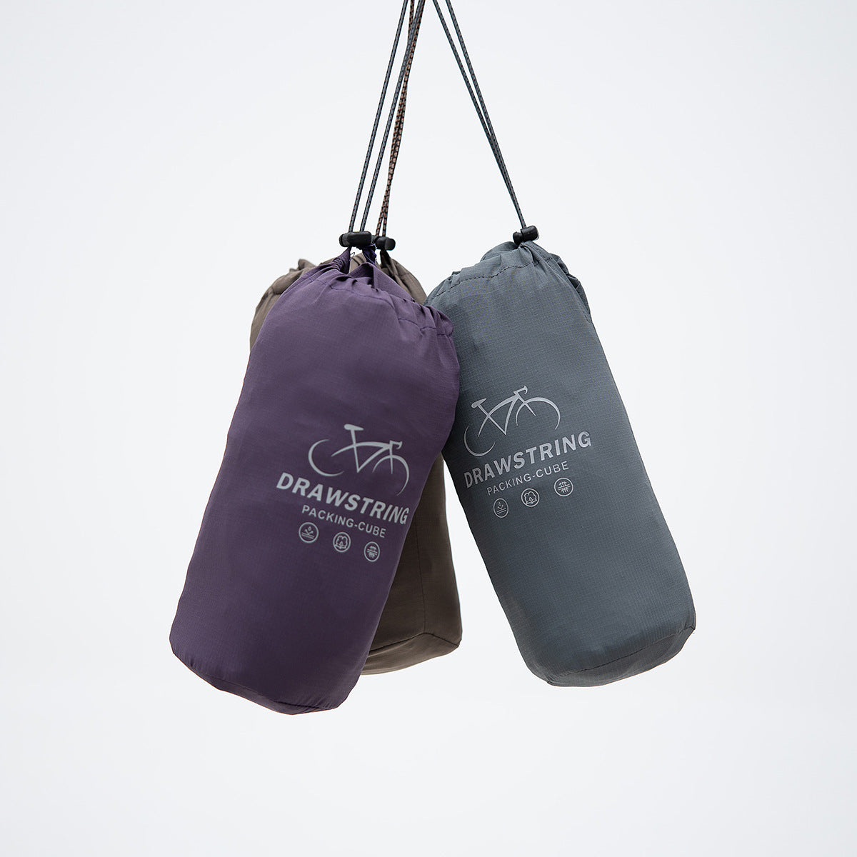 Three hanging drawstring packing bags in purple, charcoal, and taupe, printed with bicycle graphics and English text.