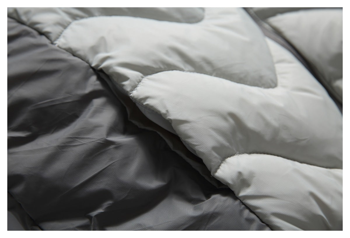 Close-up of a light gray and charcoal padded jacket with curved quilted panels.