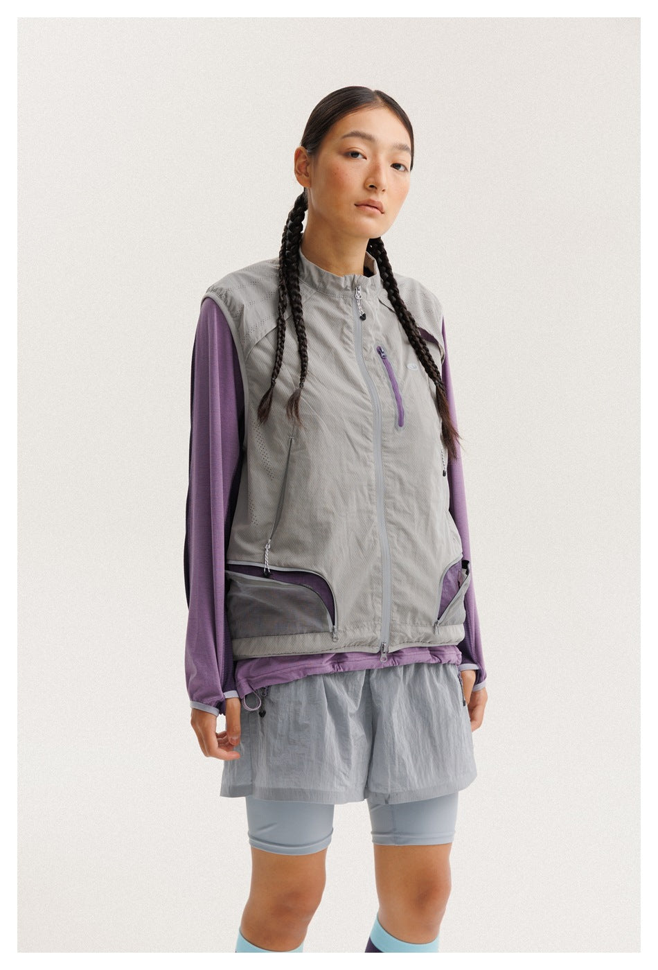 Closer front view of a model wearing a gray zip vest with mesh pockets over a purple long-sleeve top.