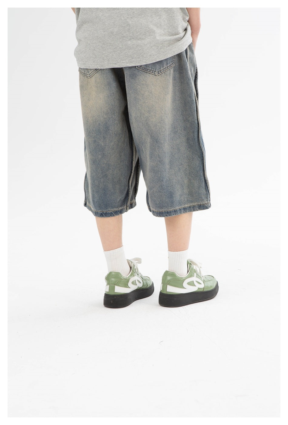 Cropped rear view of loose washed denim shorts, showing two back pockets and wide legs.