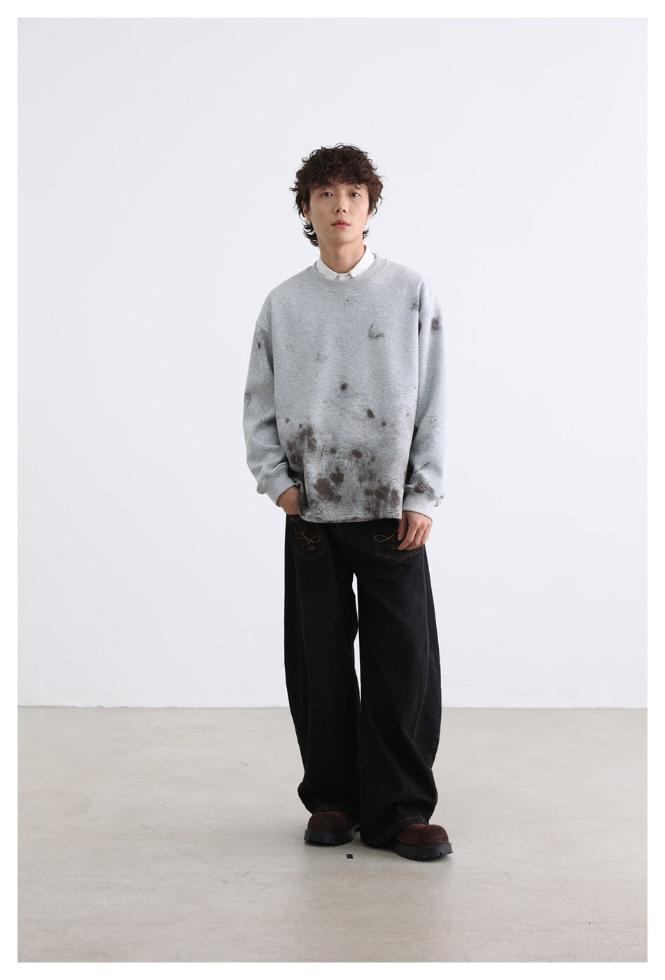 Full-length view of a model wearing a light gray distressed sweatshirt and loose black jeans.