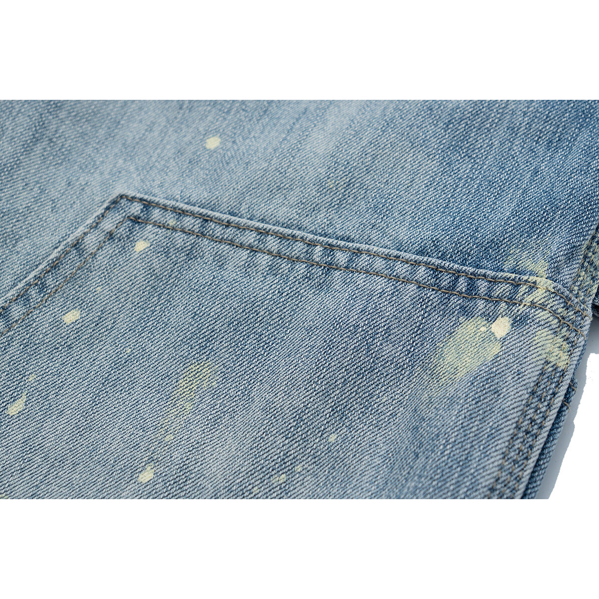 Close-up of a double-stitched utility pocket on light blue jeans, with scattered pale distressed marks.