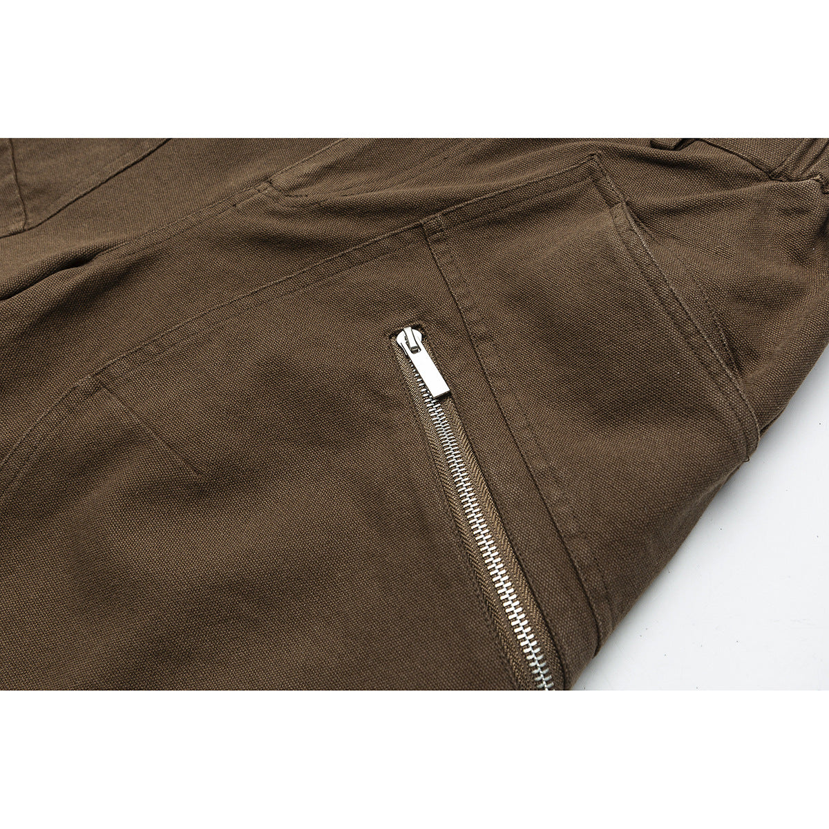 Close-up of brown trousers with a silver zipper pocket and visible panel stitching.