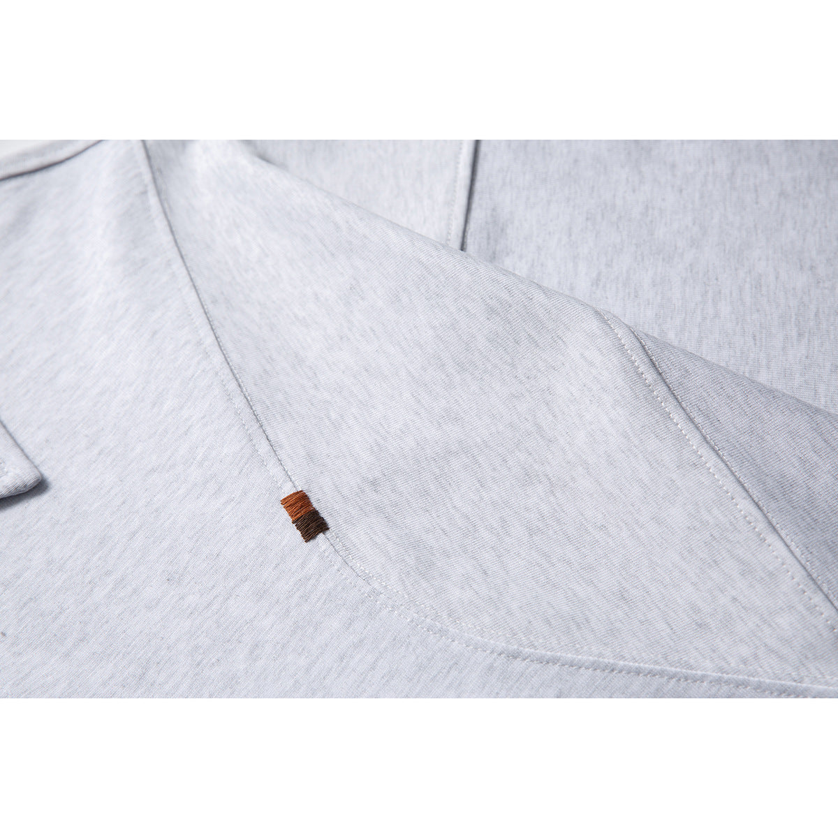 Close-up of light gray polo fabric, curved stitching, and a small brown embroidered detail.