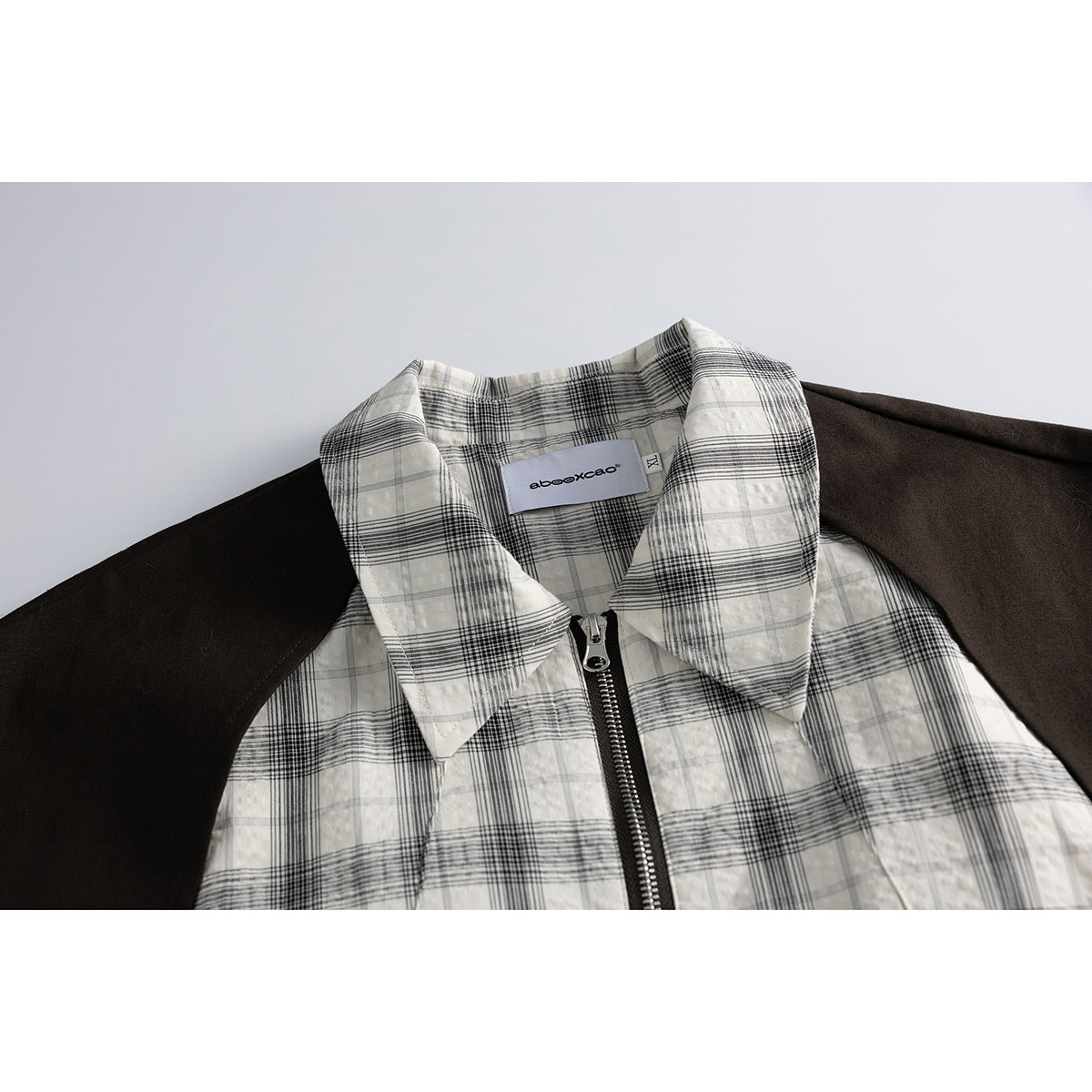 Close-up of a black-and-white plaid jacket collar and zipper, with dark brown shoulder panels and a neck label.