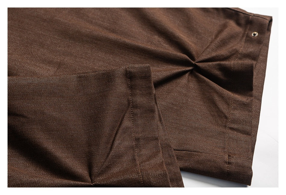 Close-up of brown trousers with a folded fabric tab, seams, and a small metal fastener.