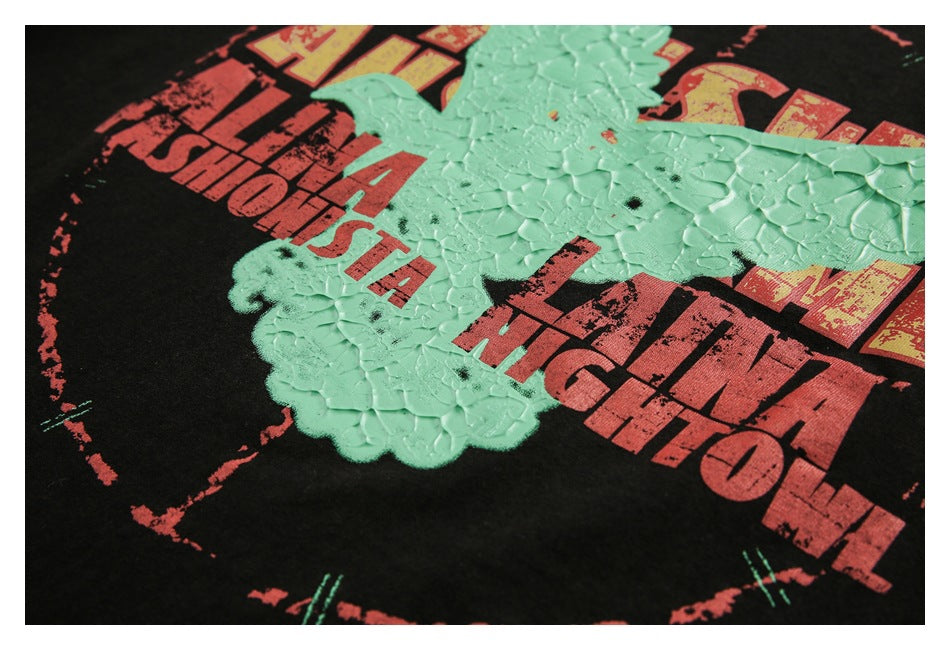 Close-up of a black garment with distressed red lettering and a raised mint-green graphic print.