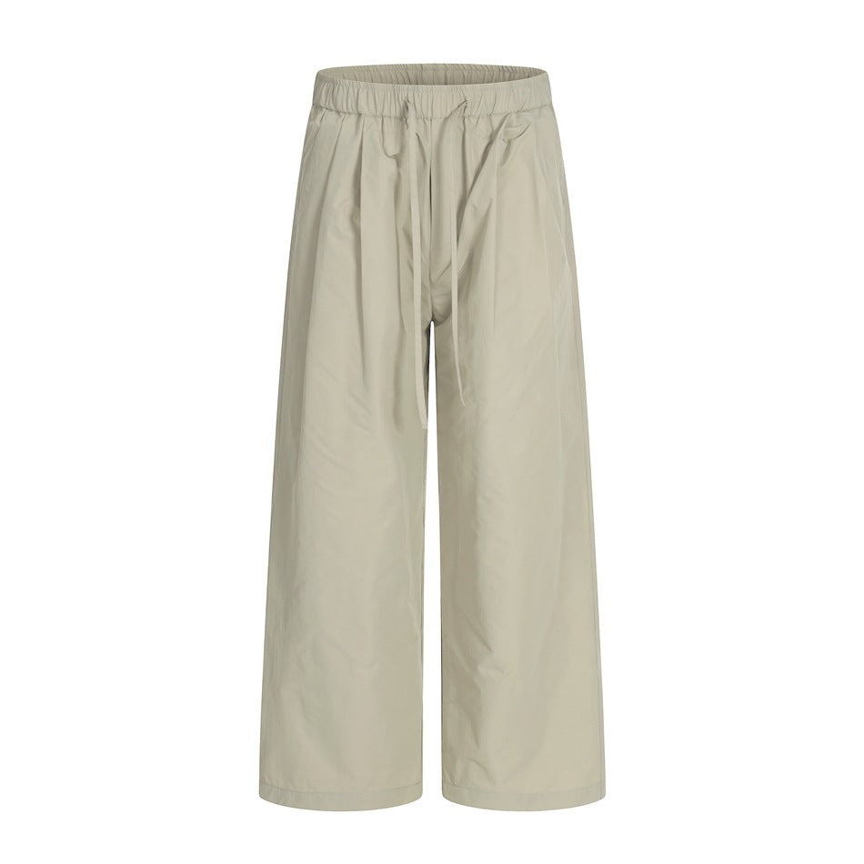Front view of light beige wide-leg trousers with an elastic waistband and long drawstrings.