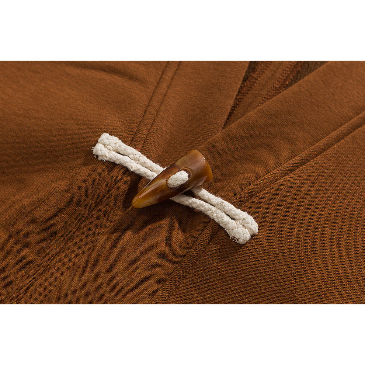 Close-up of a rust-brown vest's white braided cord loop and brown toggle closure.