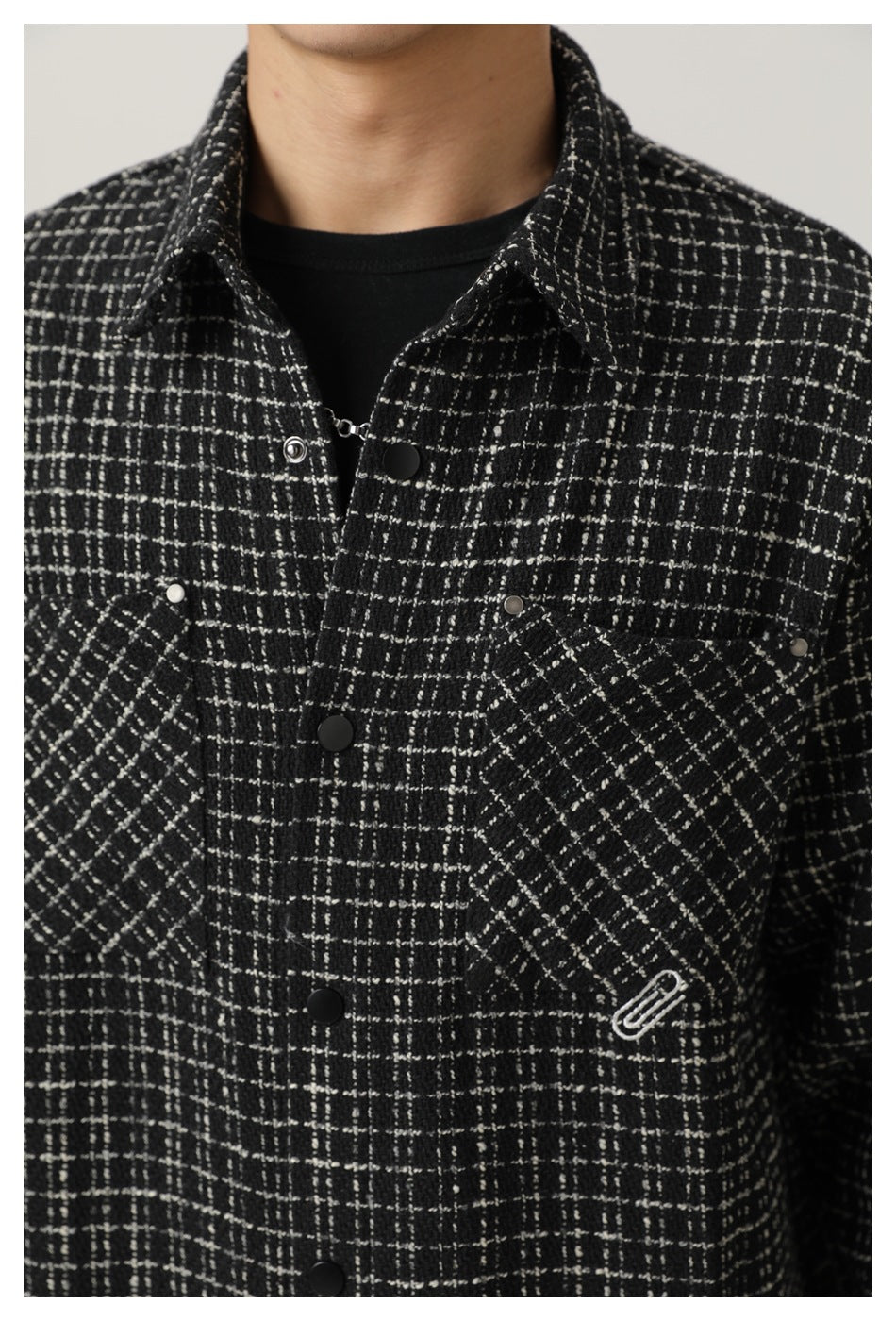 Close-up of a model wearing a black-and-white plaid snap-front shirt jacket with chest pockets and a small embroidered
