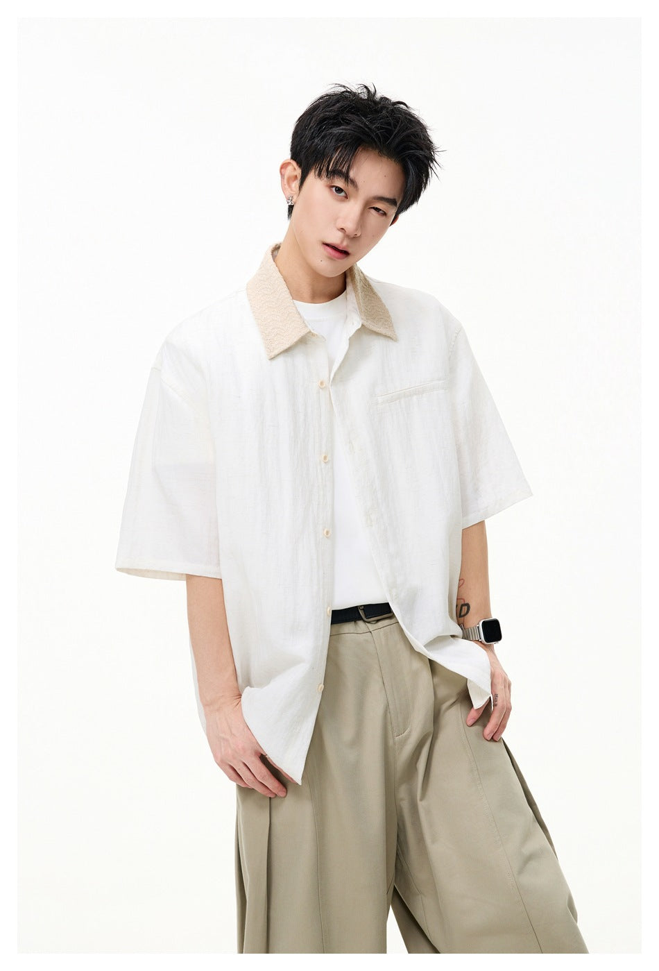 Model wearing an ivory short-sleeve shirt with a beige textured collar, open over a white tee, and khaki trousers.