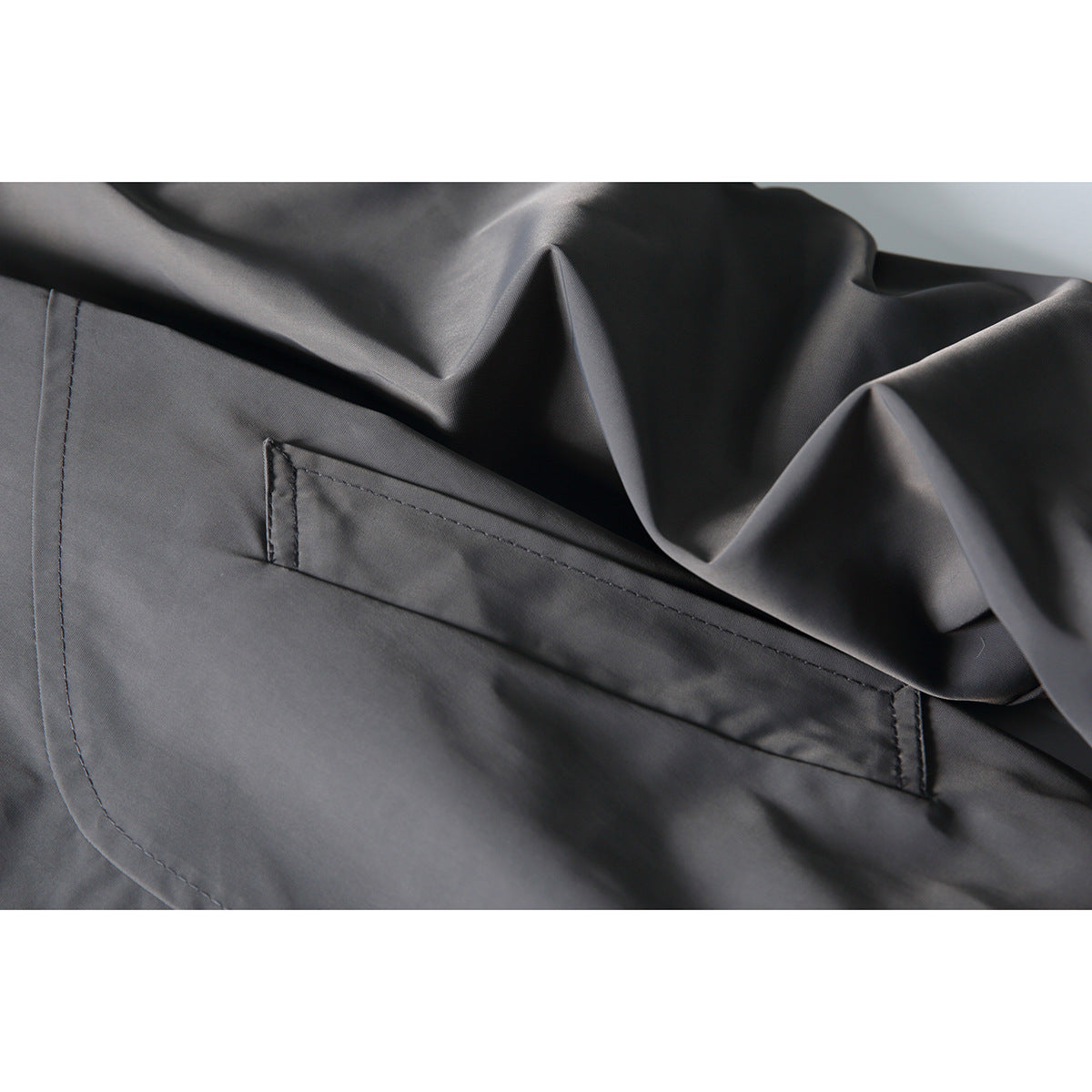Close-up of a slanted welt pocket and stitching on the charcoal jacket.