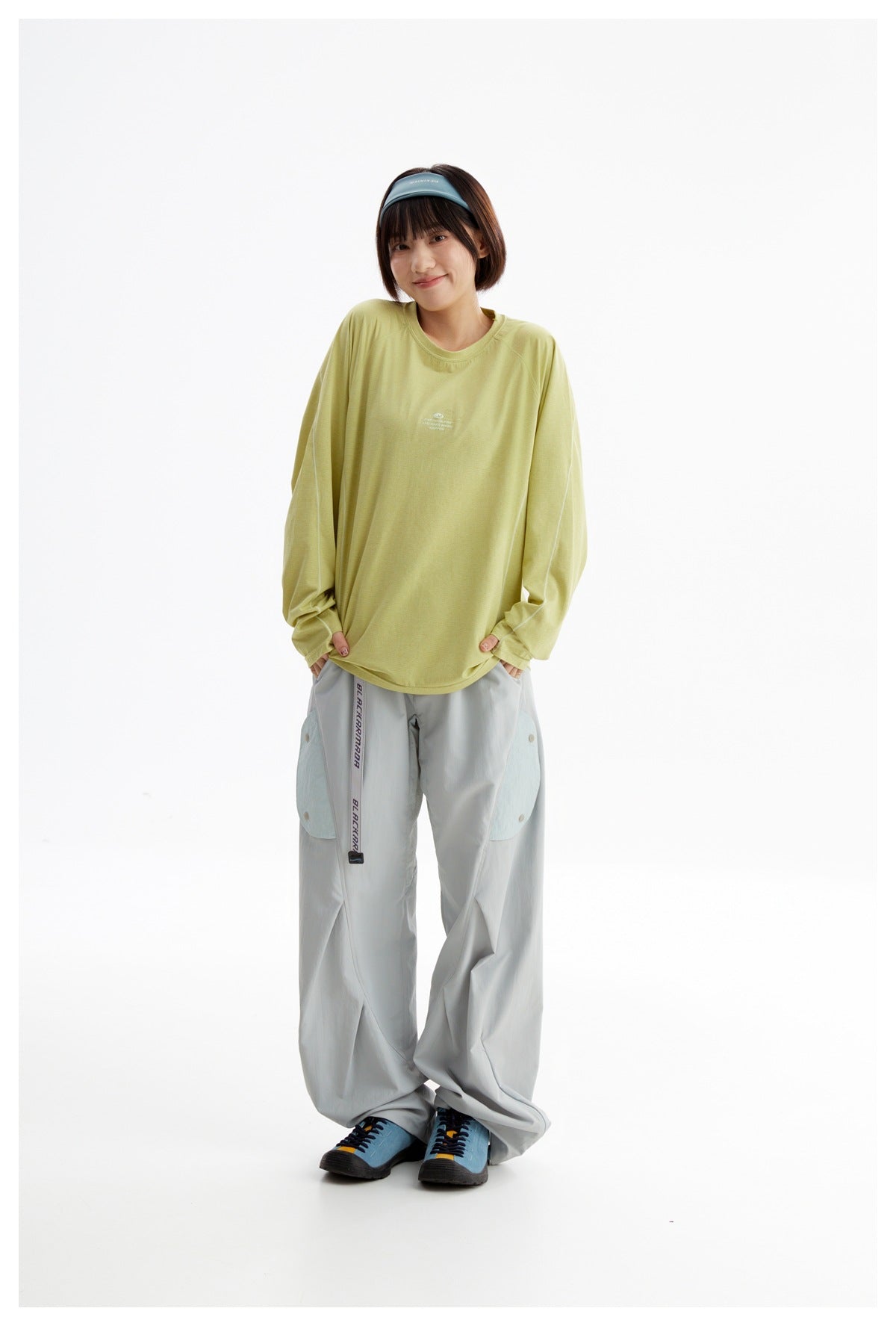 Model wearing a loose pale yellow-green long-sleeve top with light gray wide-leg pants and a blue headband.