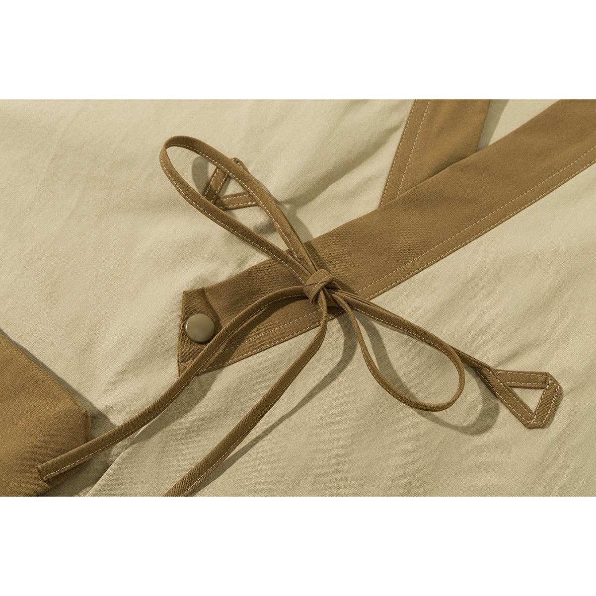 Close-up of a beige jacket's brown waist ties, loop, and buttoned tab.