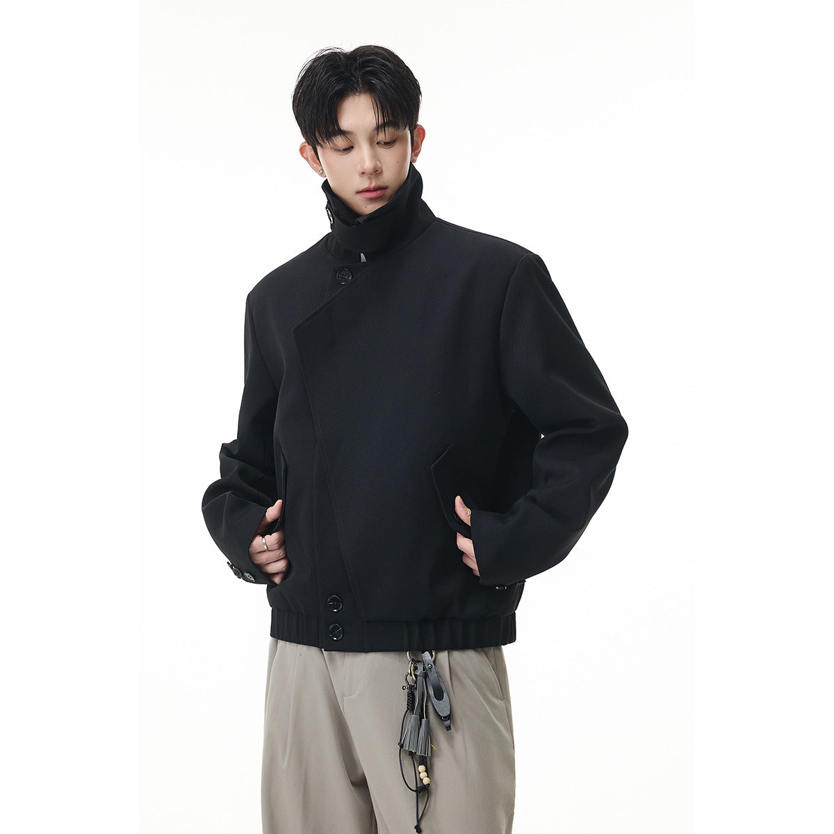 Model wearing a black high-collar jacket with an asymmetric buttoned front and ribbed hem.