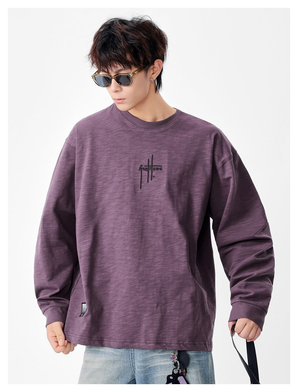 Person wearing a purple long-sleeve crew-neck top with chest lettering, sunglasses and light jeans