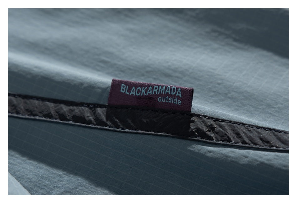 Close-up of a sewn BLACKARMADA outside label on blue-gray fabric with dark trim.