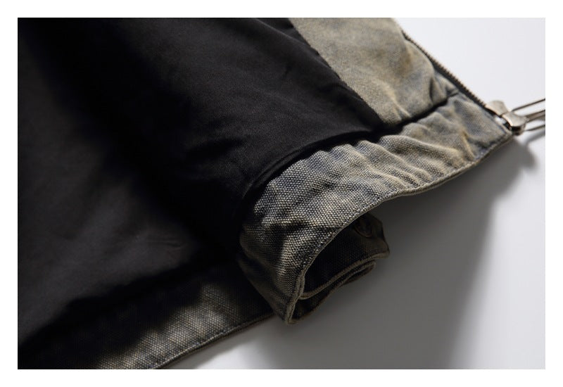 Close-up of a mottled gray-olive garment cuff with black lining and a metal zipper.