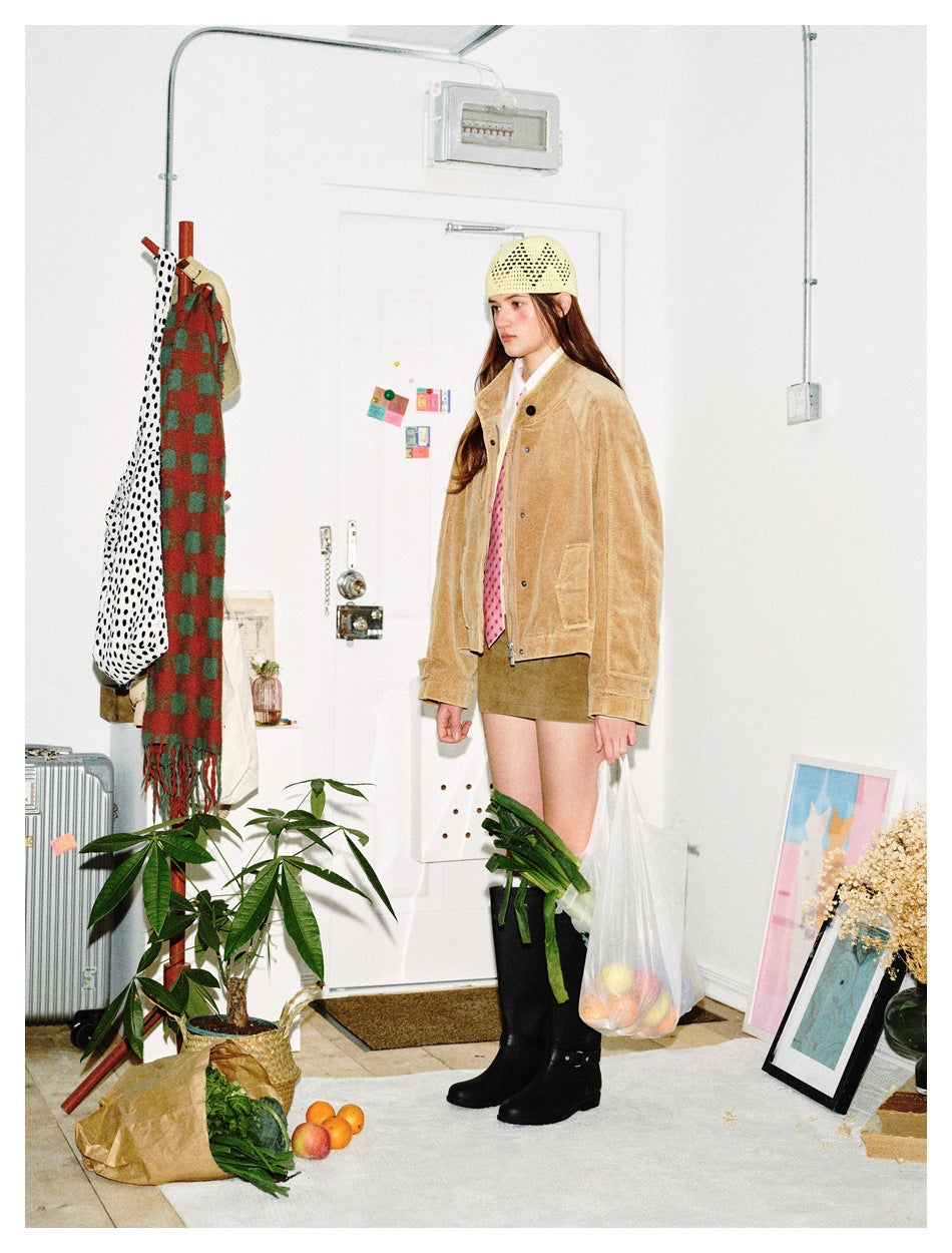 Side view of a model in a tan cropped jacket, pink-dotted shirt, olive mini skirt, cream knit cap and black boots.