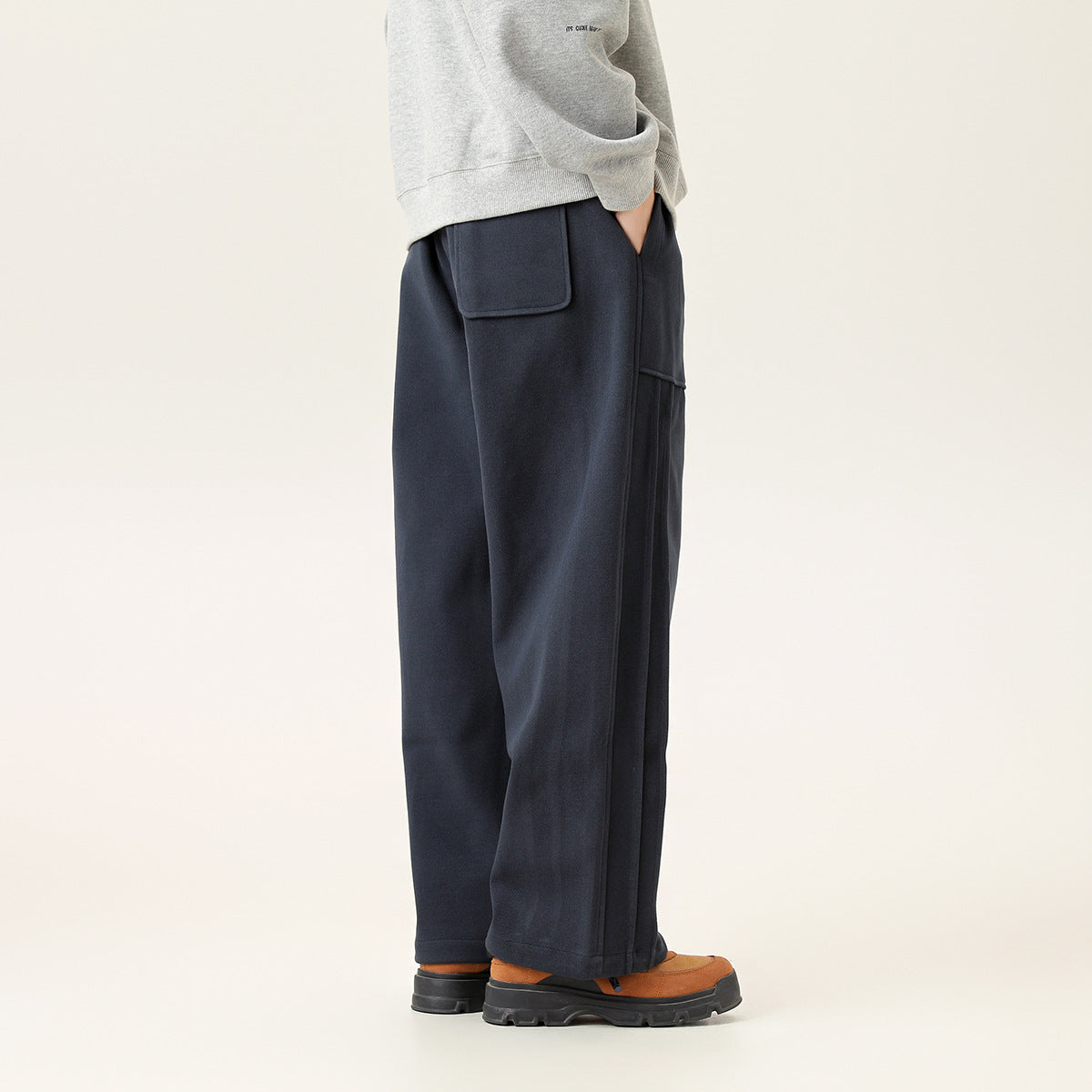 Side view of a model wearing loose dark navy pants with a large pocket and straight legs.