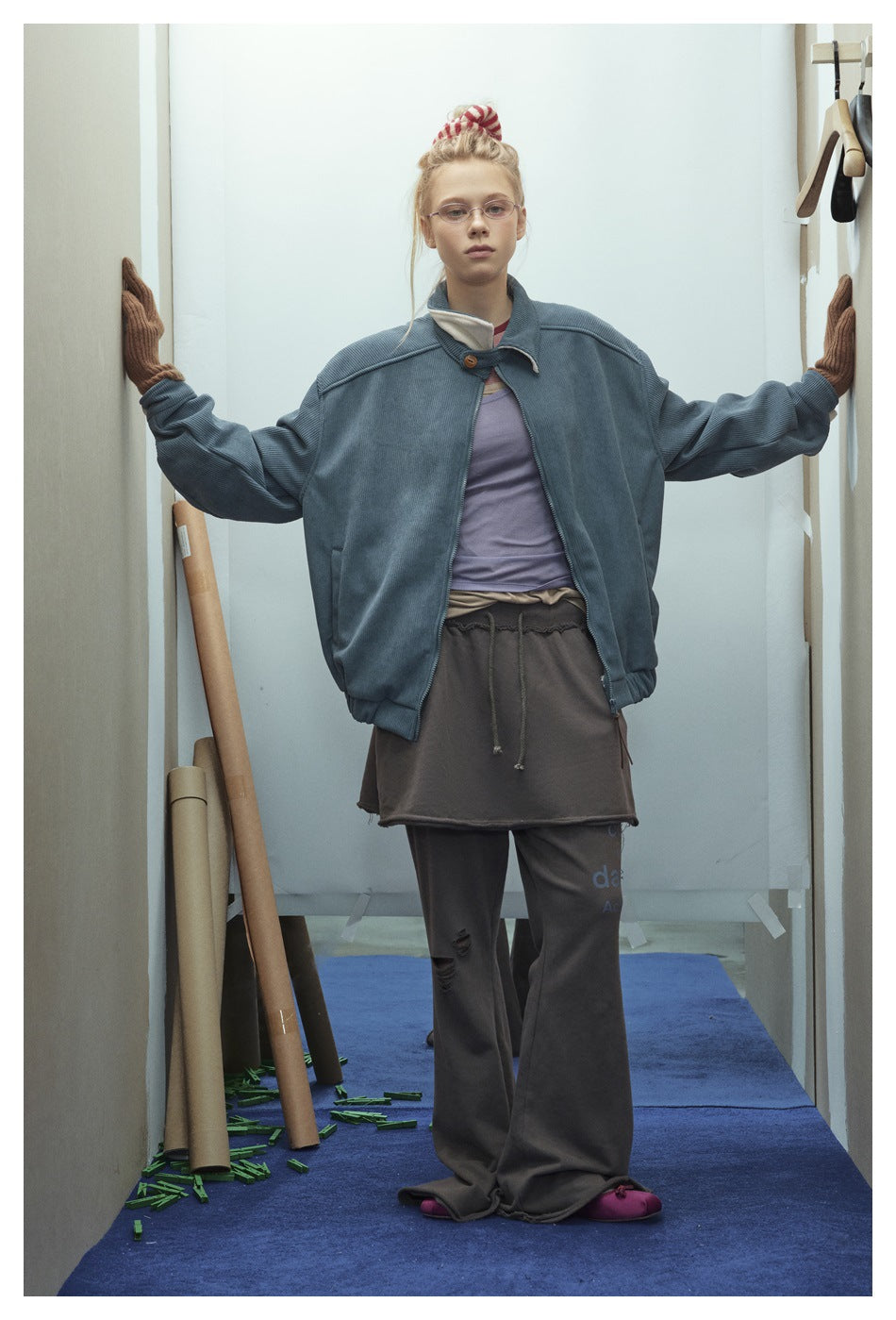 Model facing forward with arms outstretched, wearing an open blue-gray ribbed jacket and brown gloves.