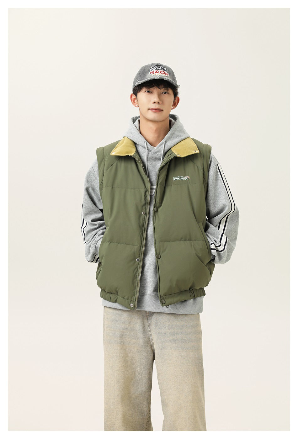 Model wearing an olive green puffer vest with a mustard collar over a gray striped-sleeve hoodie