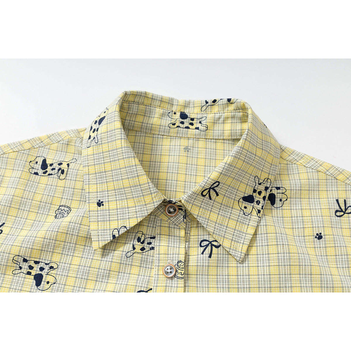 Close-up of a pointed collar on a yellow plaid shirt with navy animal and bow prints and brown-rimmed buttons.