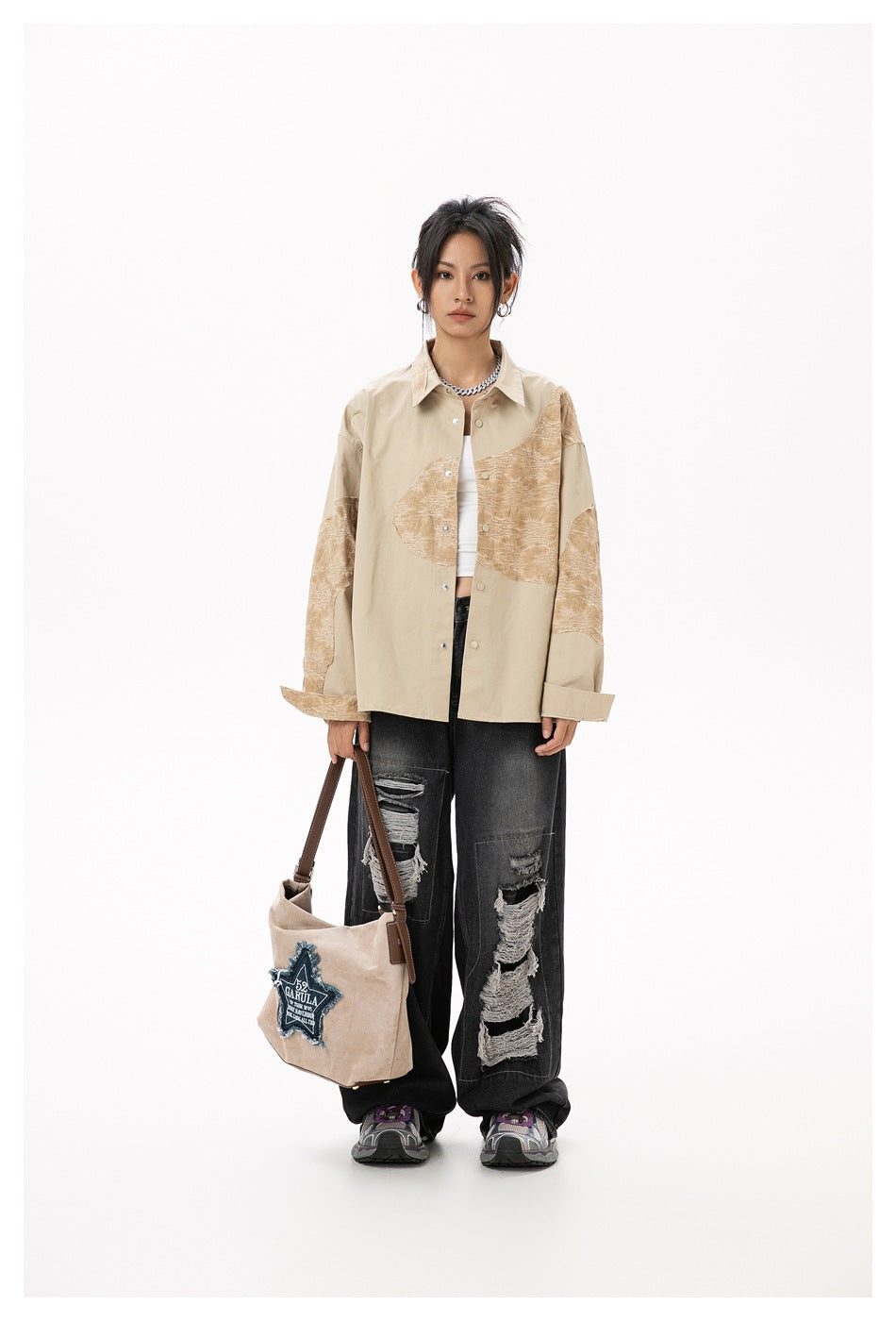 Model wearing a loose beige button-up shirt with tan textured panels, black distressed jeans, and carrying a tote.