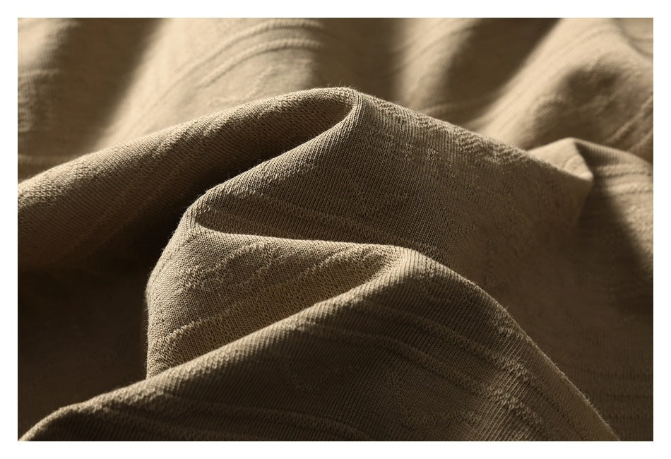 Extreme close-up of the tan shirt's textured patterned fabric gathered into folds.