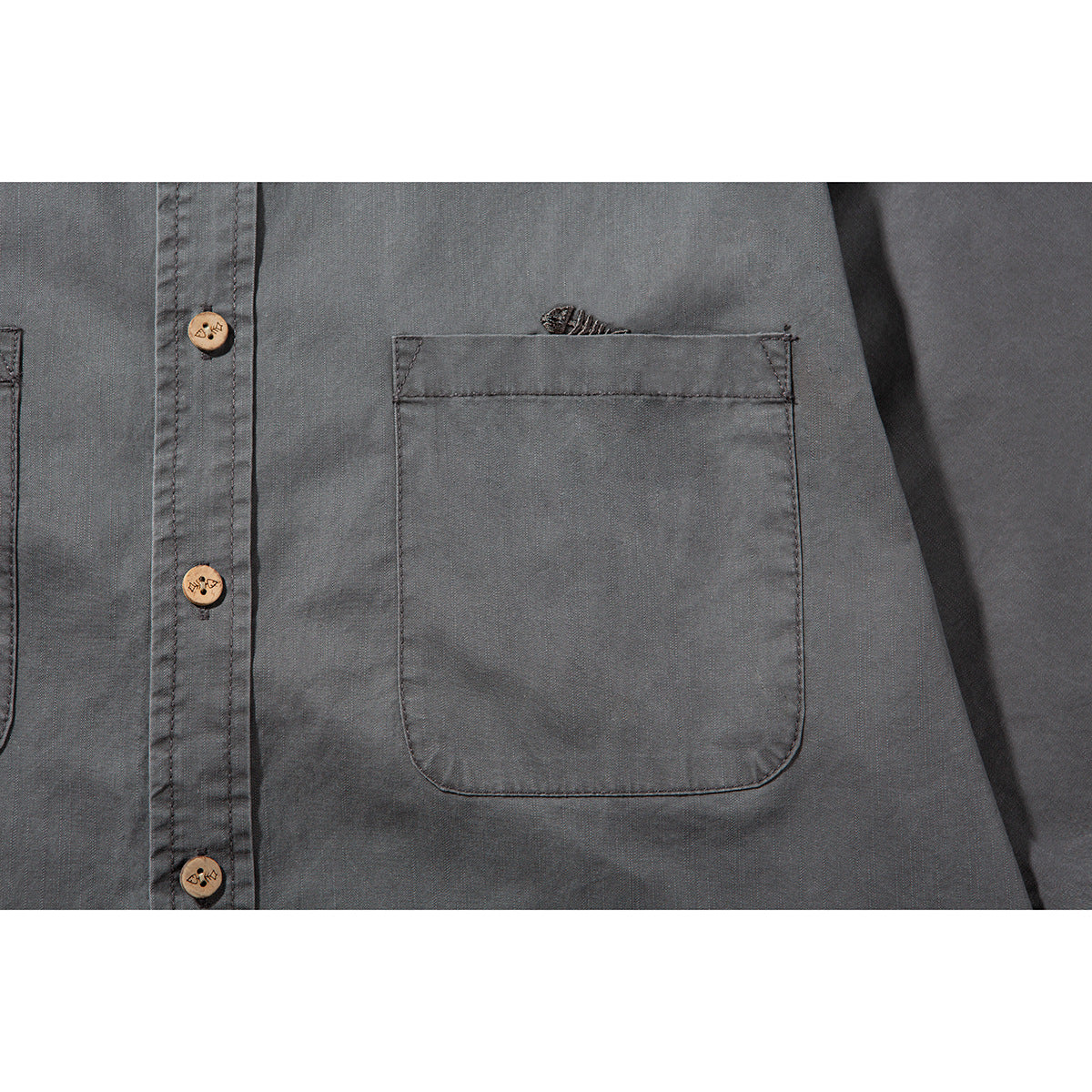 Close-up of a chest pocket, wooden buttons, and stitching on a charcoal-gray shirt.