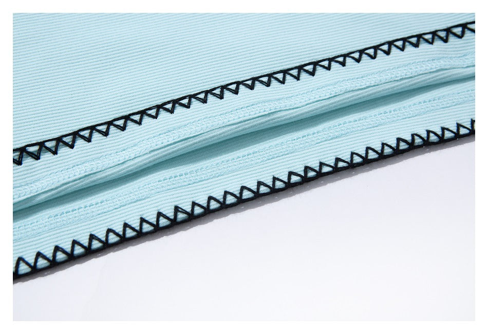 Close-up of light blue fabric edges finished with black zigzag stitching.