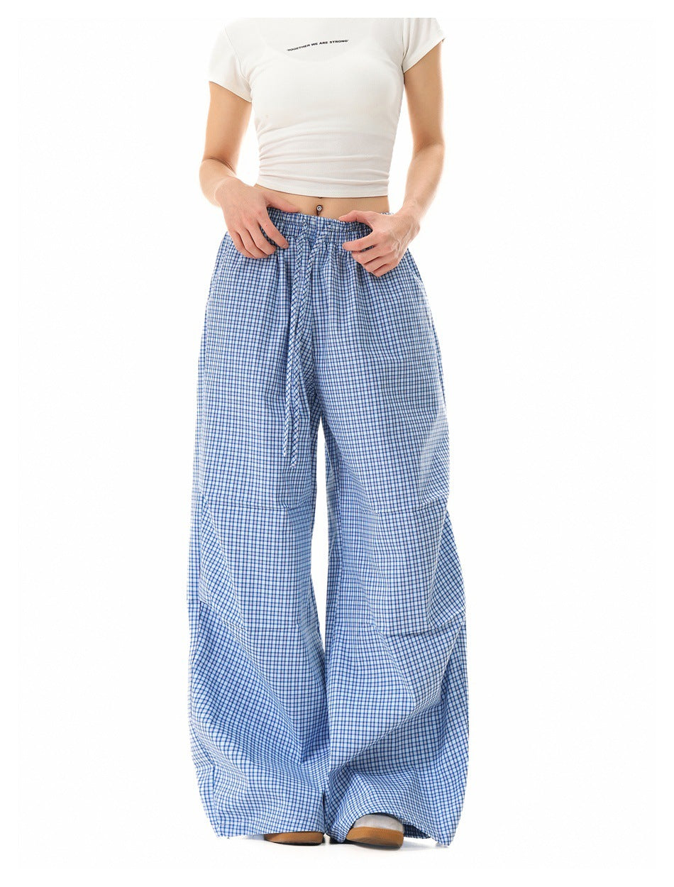 Model with hands at the waistband wearing blue plaid wide-leg pants and a white cropped tee, cropped view