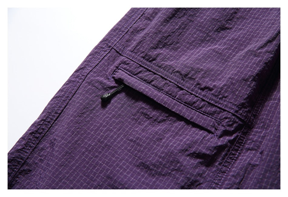 Close-up of purple grid-pattern shorts showing a flap pocket with a small button.
