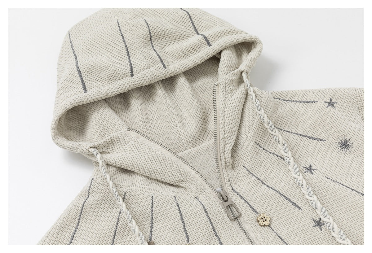 Close-up of the ivory jacket hood, braided drawcord trim, zipper, and gray celestial motifs.