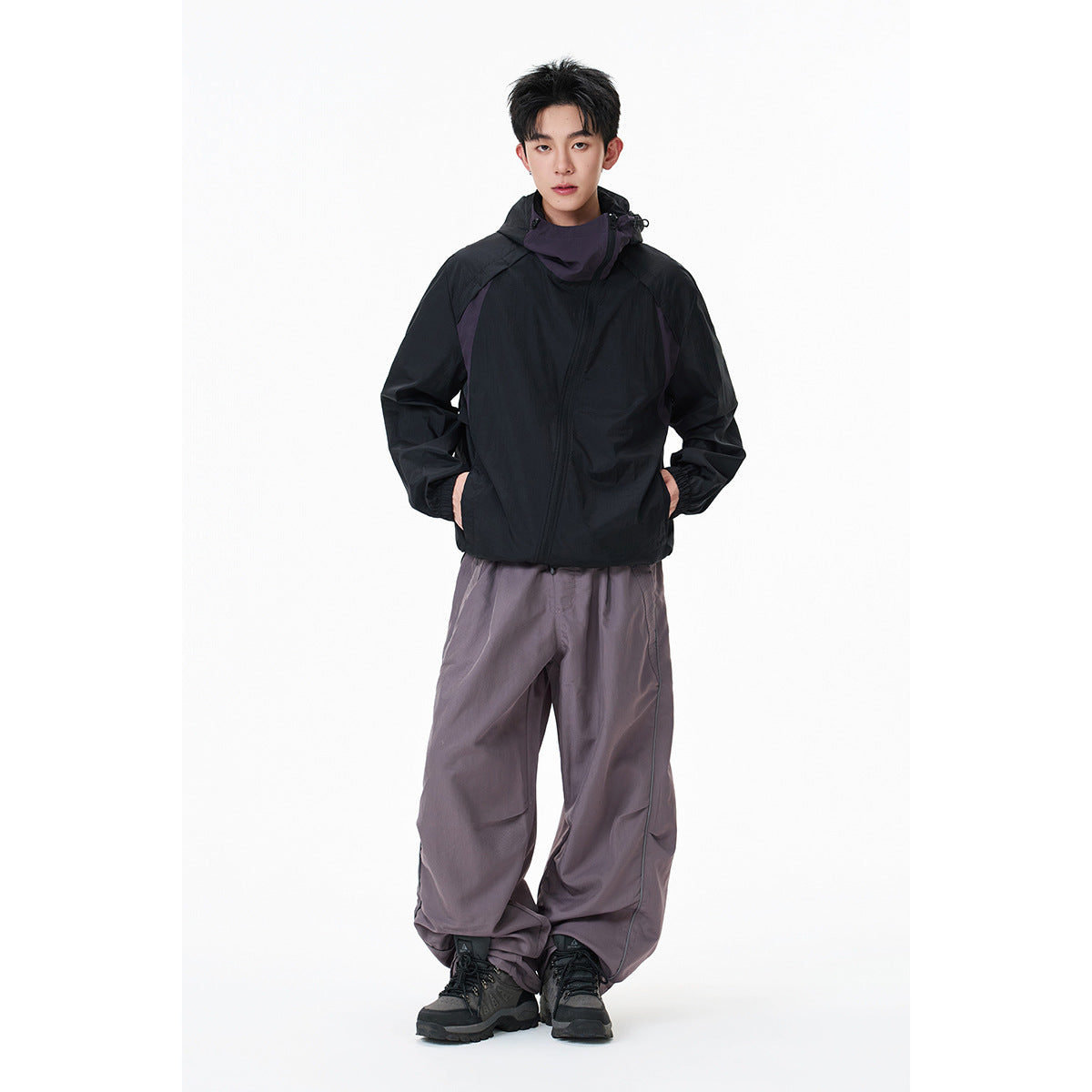 Model wearing a black hooded windbreaker with purple panels and loose gray-purple trousers.