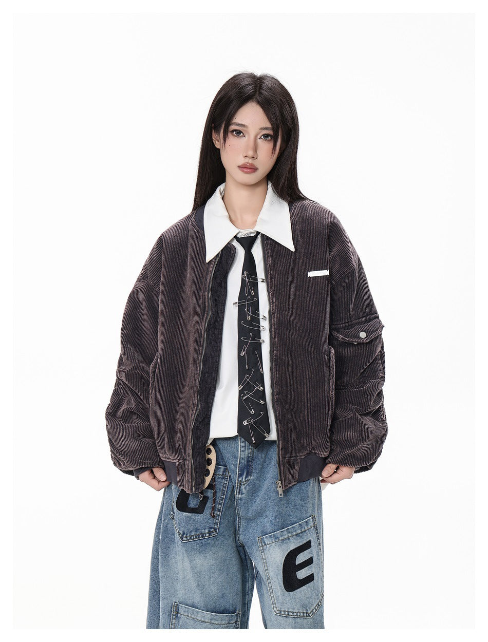Model in dark purple-gray corduroy bomber jacket worn open over white collared shirt and safety-pin tie, close-up