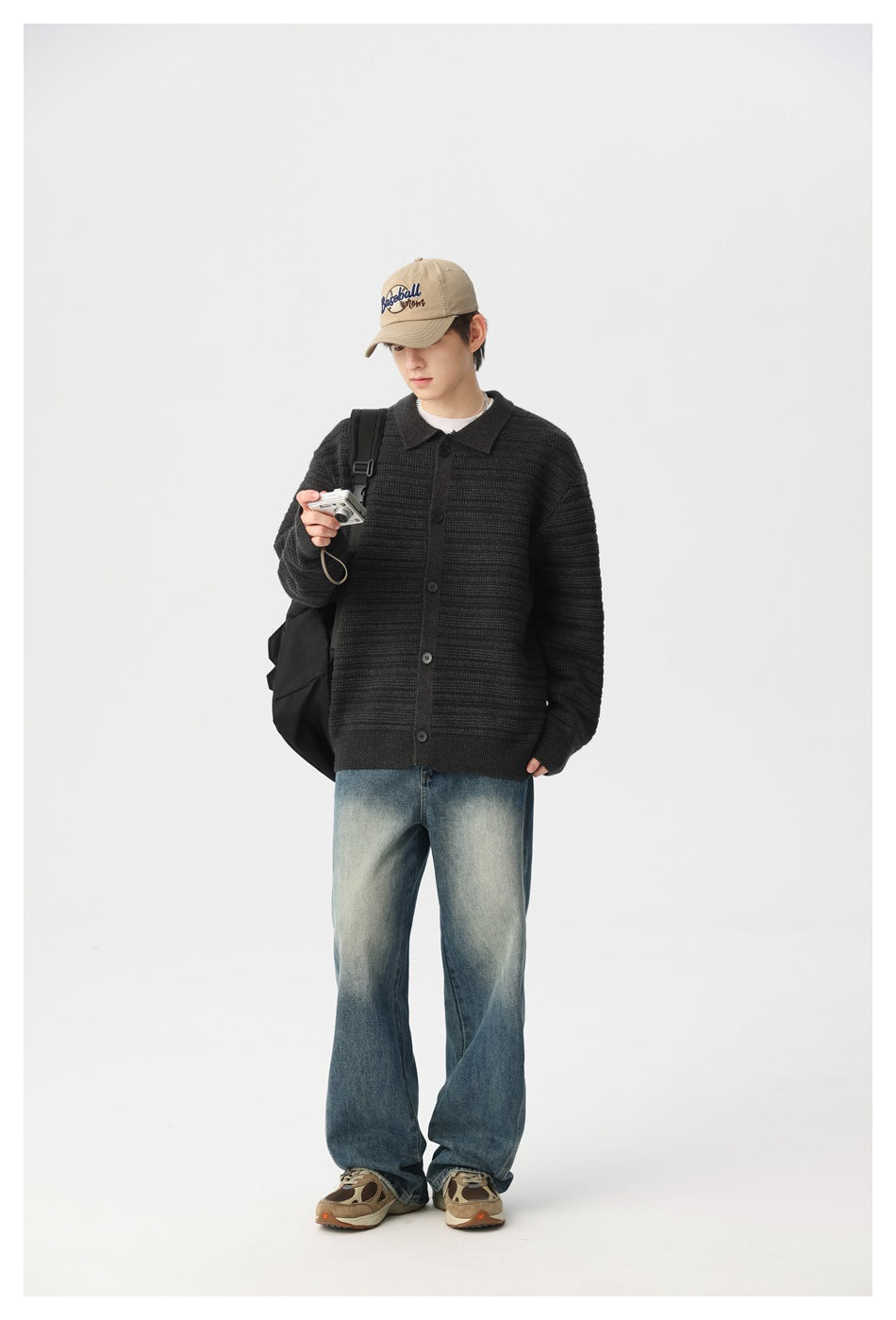 Model wearing a dark charcoal button-front knit cardigan with a collar, styled with loose jeans and a beige cap.