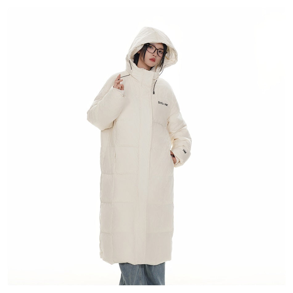Model wearing a cream long hooded puffer coat zipped closed with the hood up, over blue jeans
