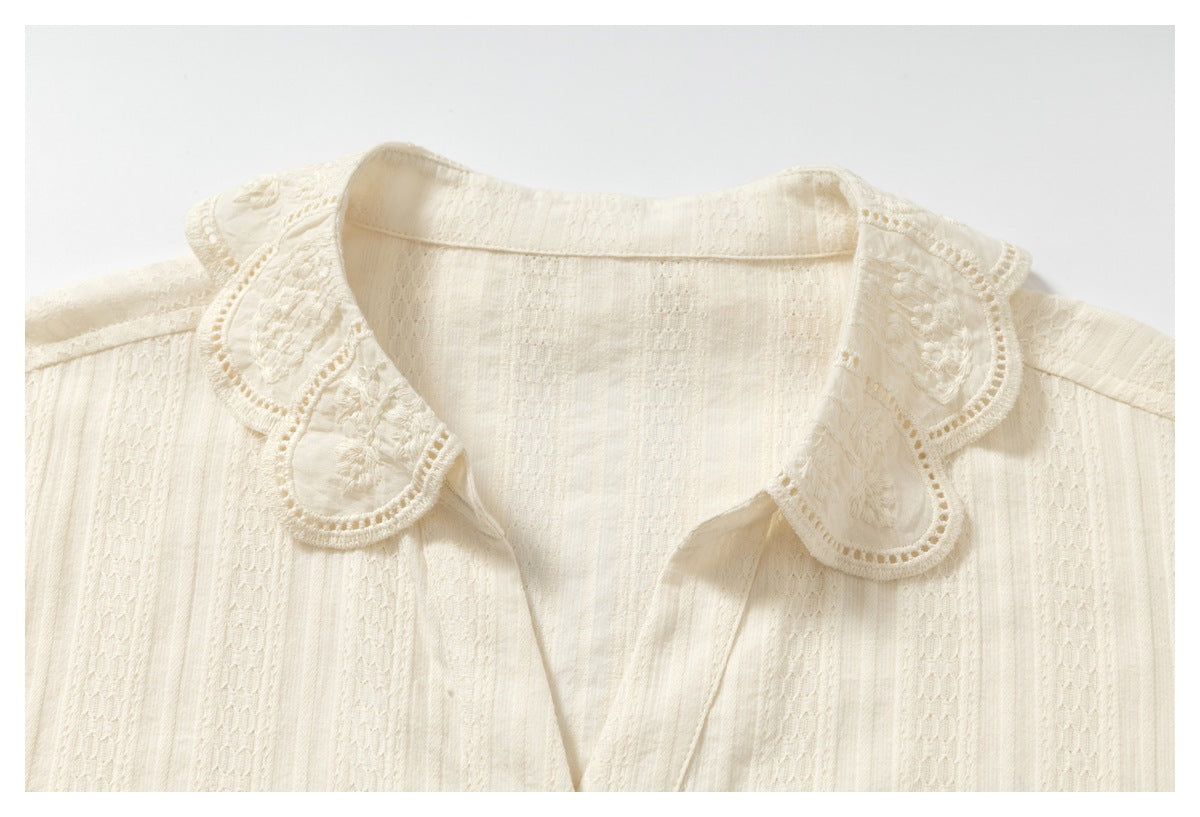 Close-up of an ivory shirt’s floral embroidered scalloped collar and textured fabric.