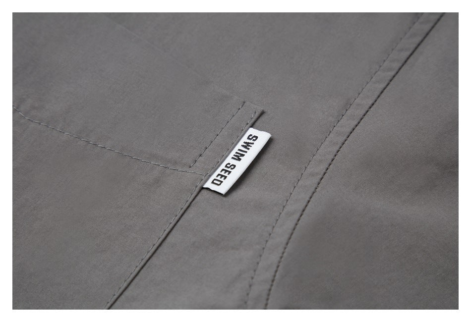 Close-up of a SWIM SEED label sewn beside the gray shirt's pocket.