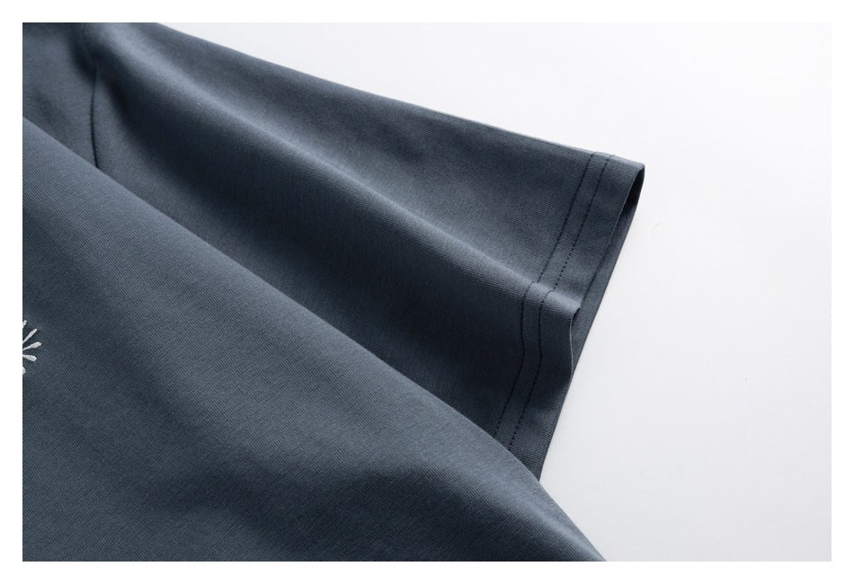 Close-up of a dark slate-gray sleeve with a double-stitched cuff; part of a white embroidered motif is visible.