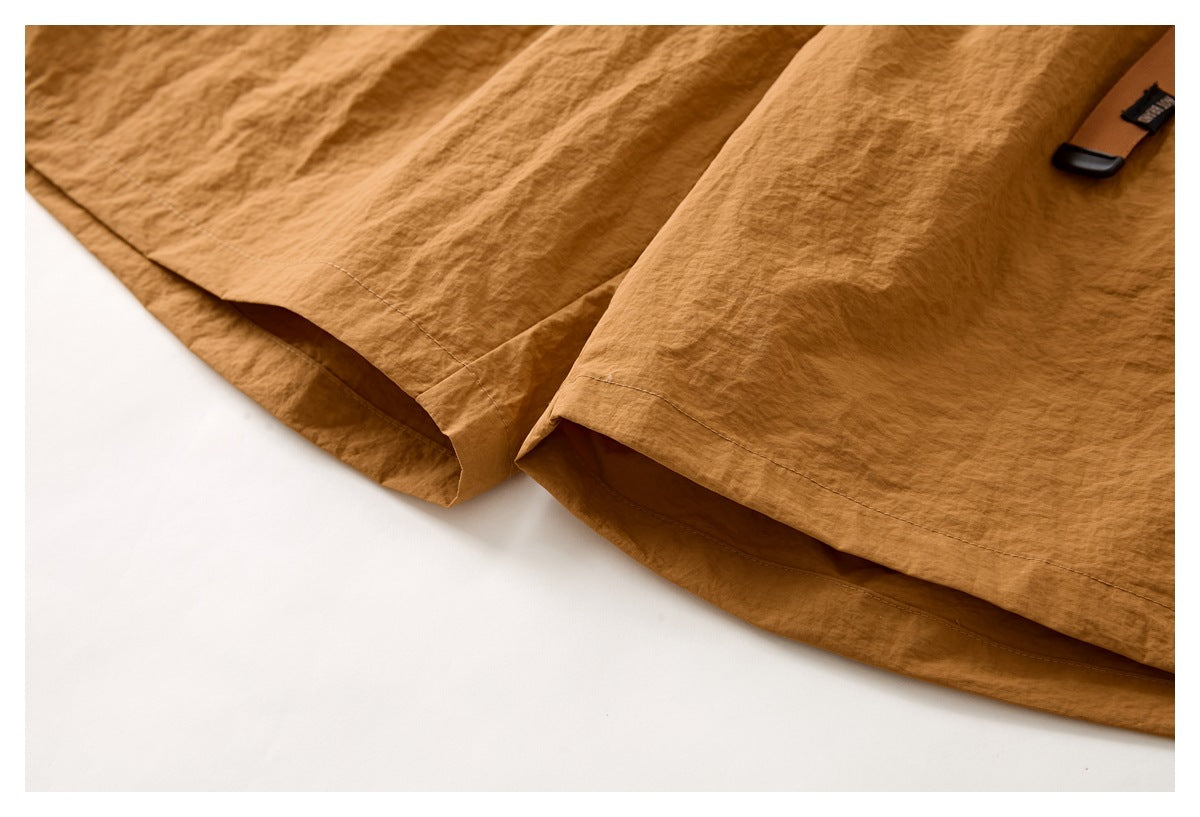 Close-up of the rust-brown shorts' leg openings and stitched hems, with part of the belt end visible.