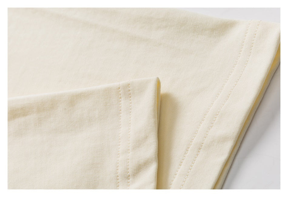 Close-up of cream garment fabric and a folded edge showing parallel rows of stitching.