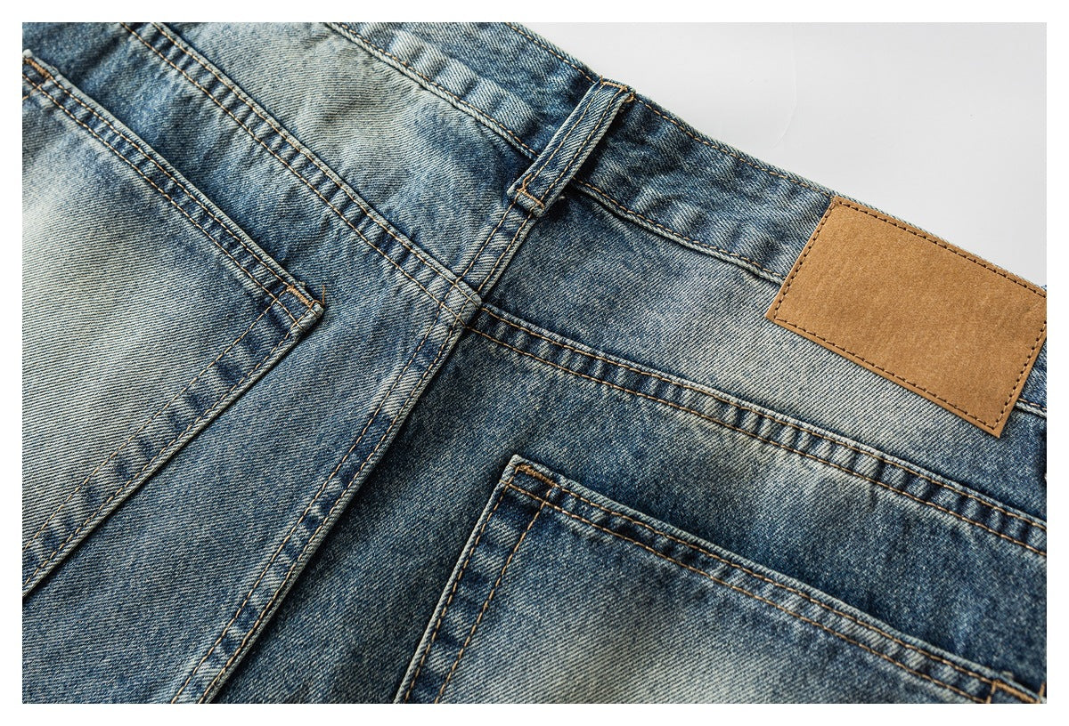 Close-up of the back waistband of blue jeans, showing a belt loop, pocket seams, and a blank tan patch.