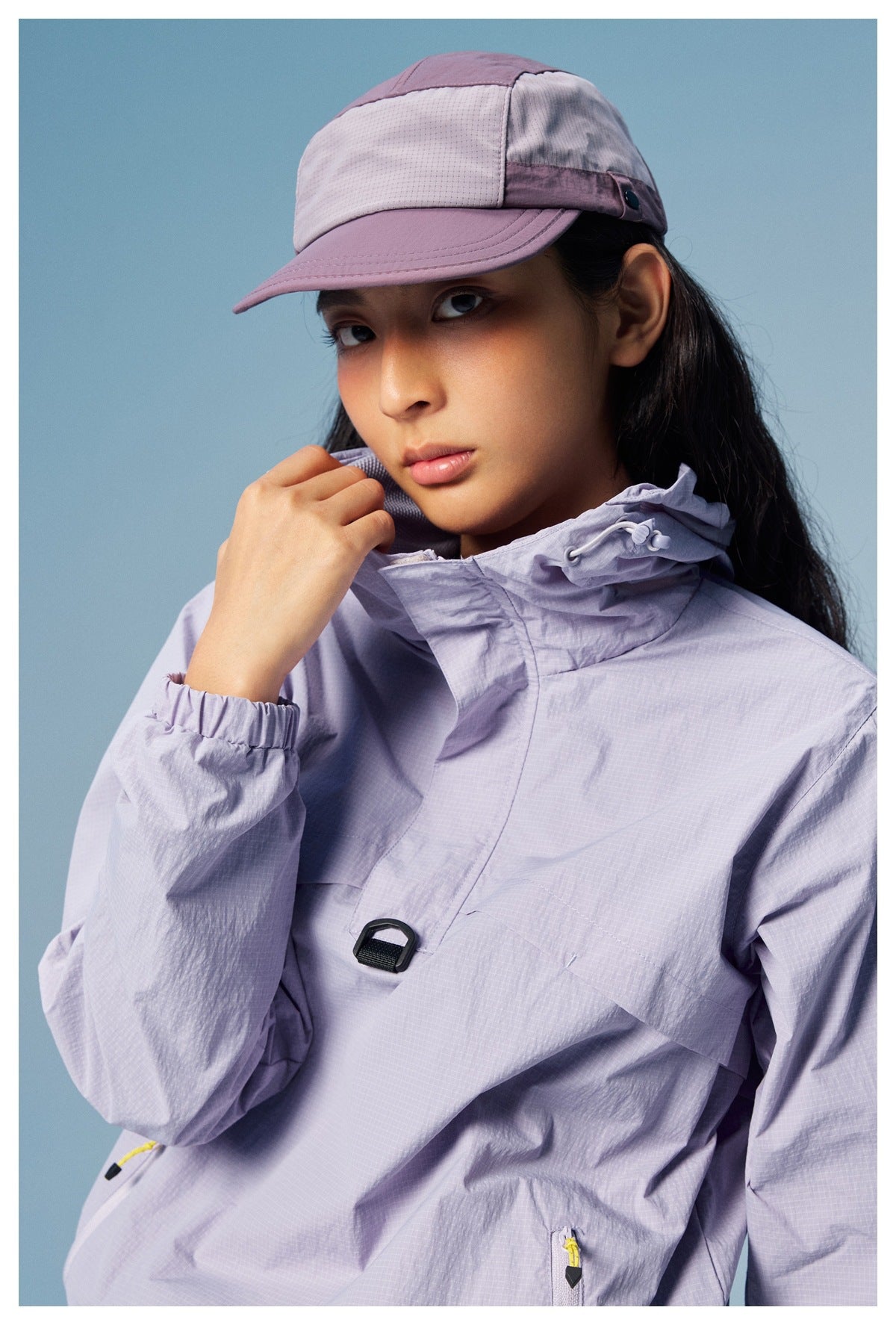 Close-up of a light lavender hooded jacket's adjustable hood and front buckle, with a matching color-block cap.
