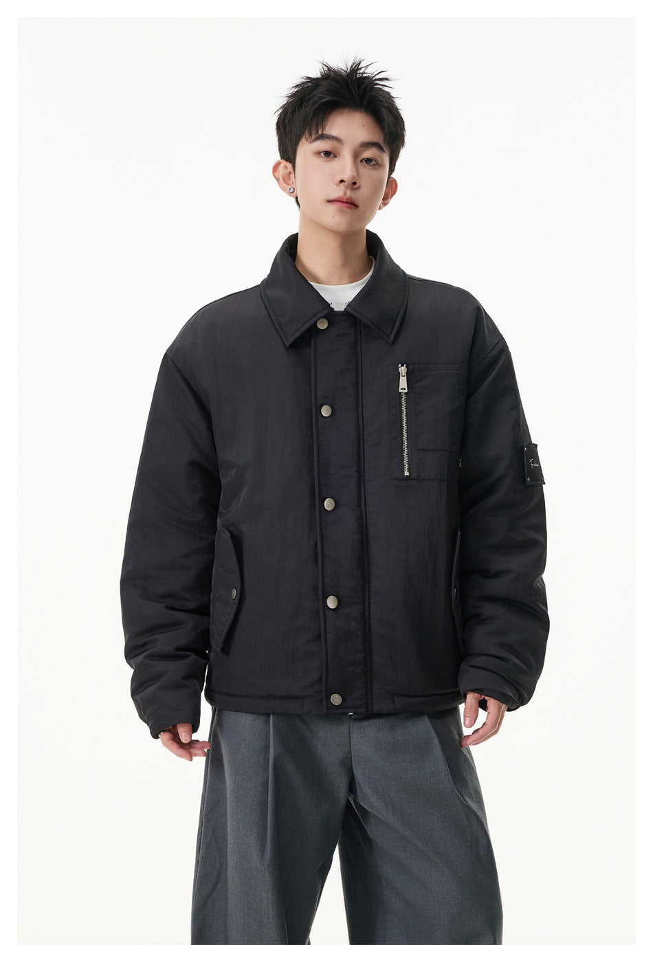 Model wearing black padded collared jacket with snap front and zip chest pocket, gray trousers, close-up