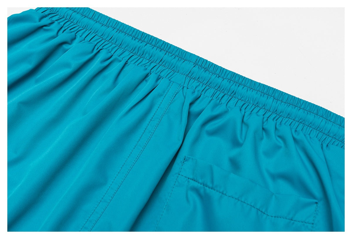 Close-up of turquoise shorts showing the elastic waistband, center seam, and rear patch pocket.