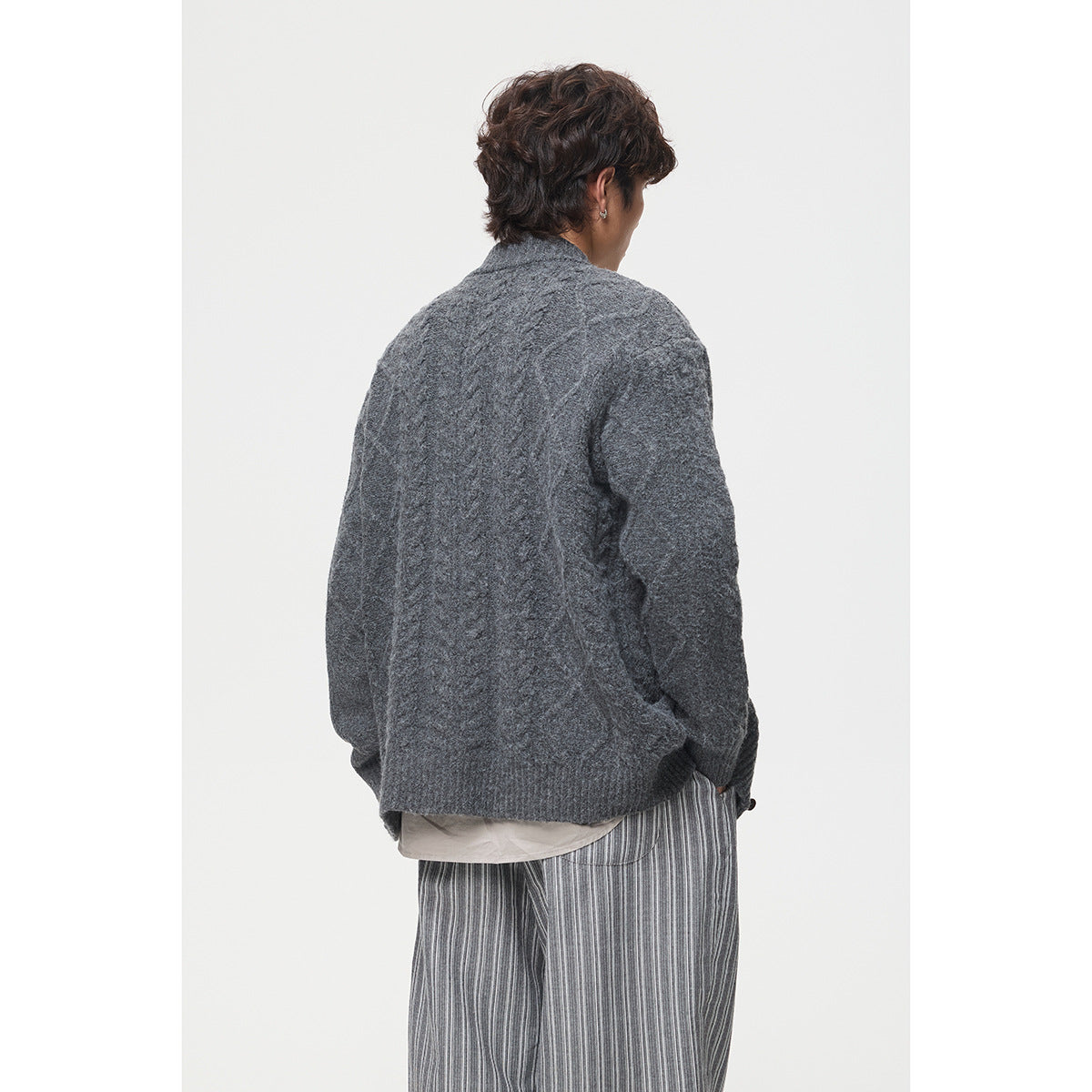 Back view of a model wearing a charcoal cable-knit cardigan with ribbed cuffs and hem.