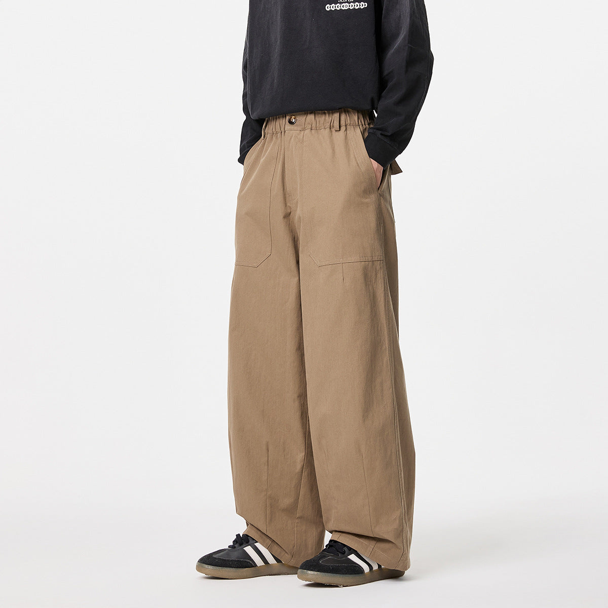 Front view of a model wearing tan wide-leg trousers with an elastic waist, button closure and large front patch pockets.