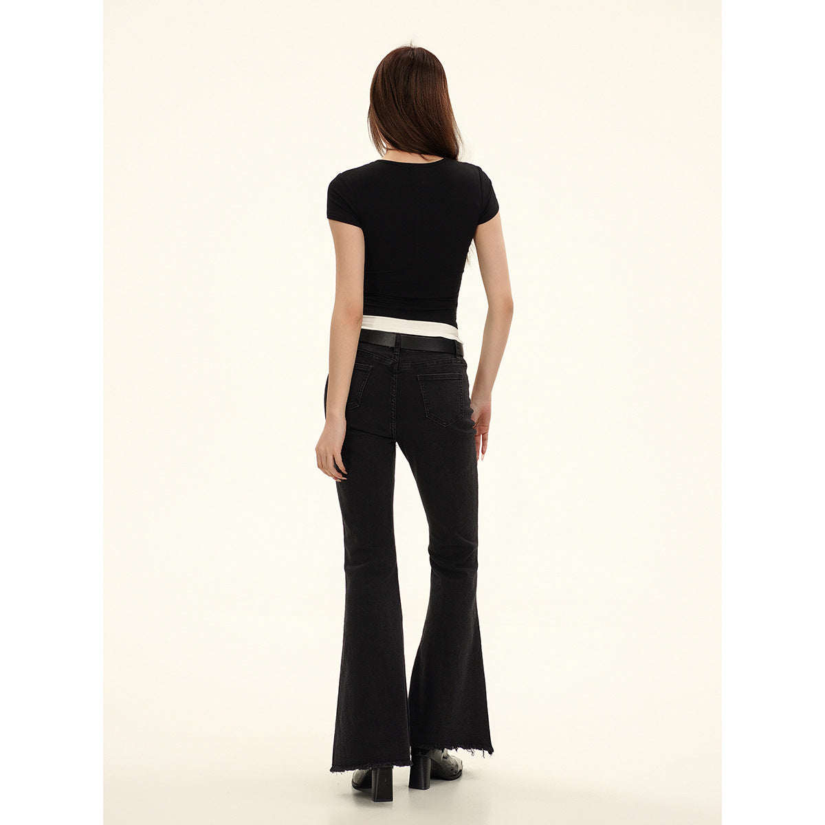 Back view of a model wearing a fitted black short-sleeve top and black flared jeans with back pockets.